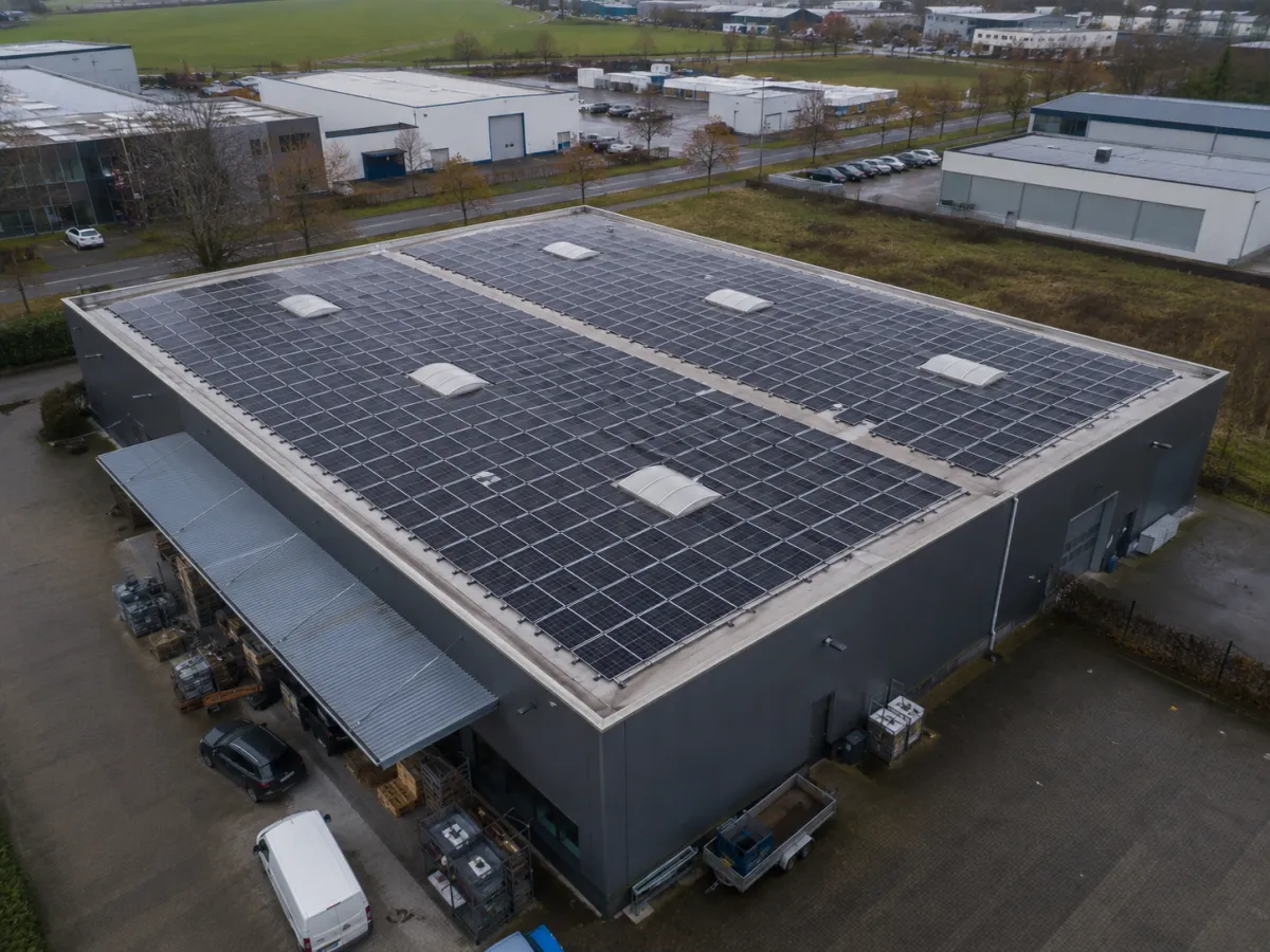 Moderne Gewerbehalle mit großflächiger Photovoltaik-Aufdachanlage auf dem Flachdach aus der Vogelperspektive